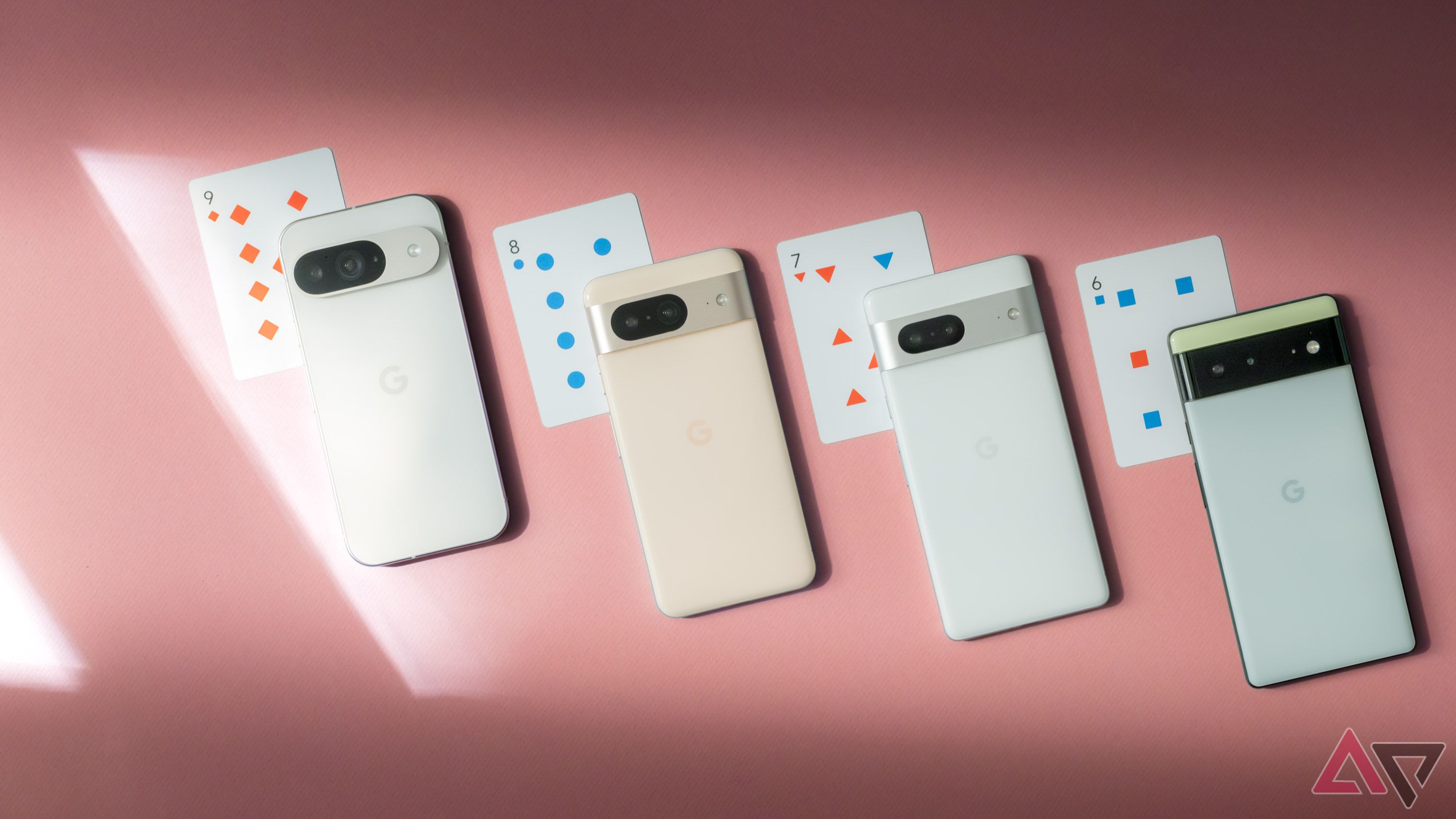 Four Google Pixel phones arranged on a pink surface next to playing cards