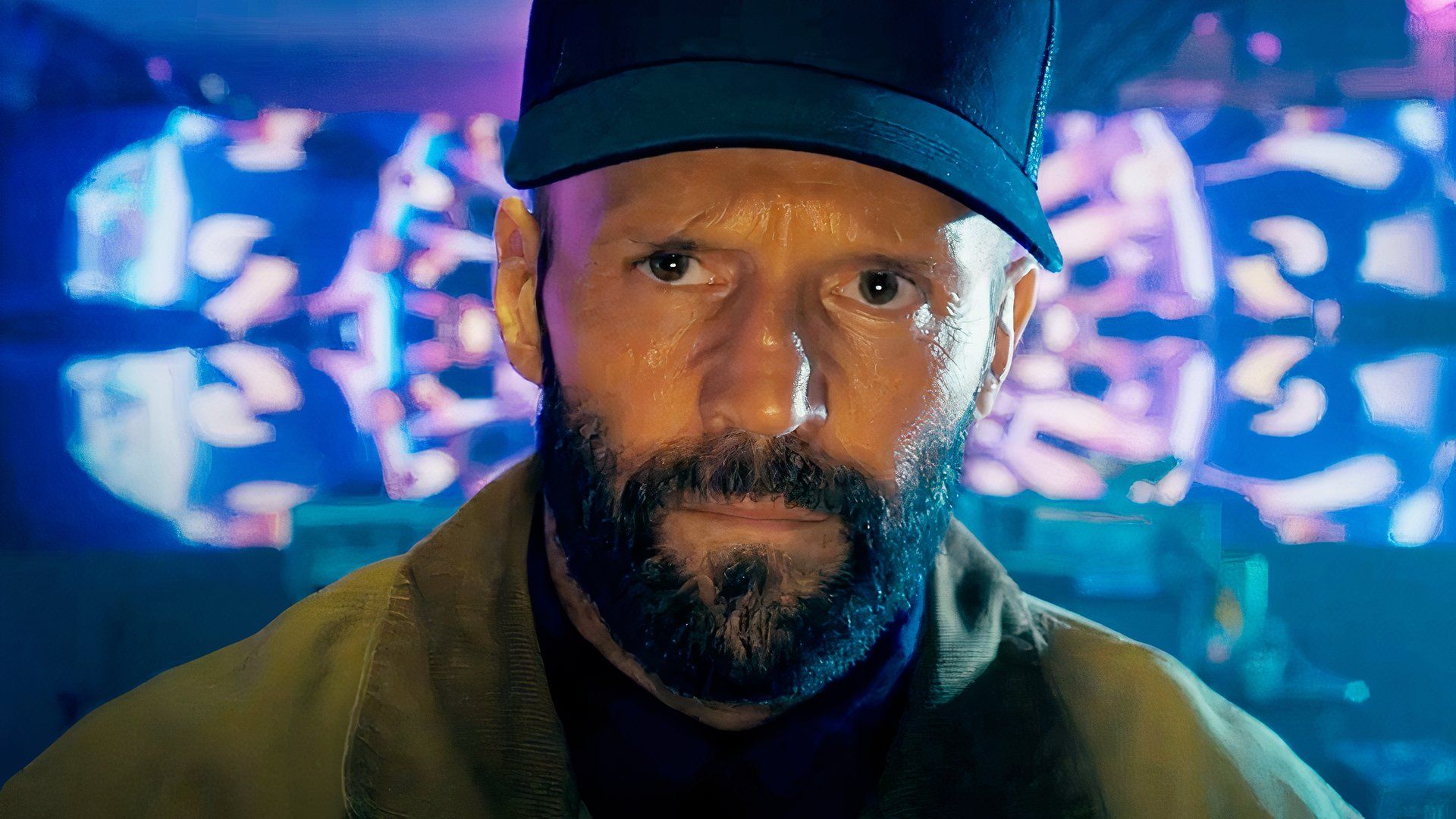 Jason Statham wears a hat with a big screen in the background in the film the beekeeper