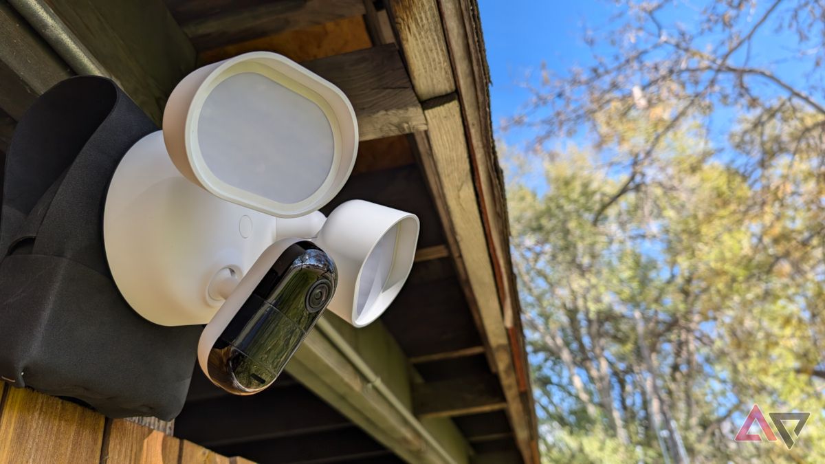 Arlo Wired Floodlight Camera under overhang with fence and tree in background