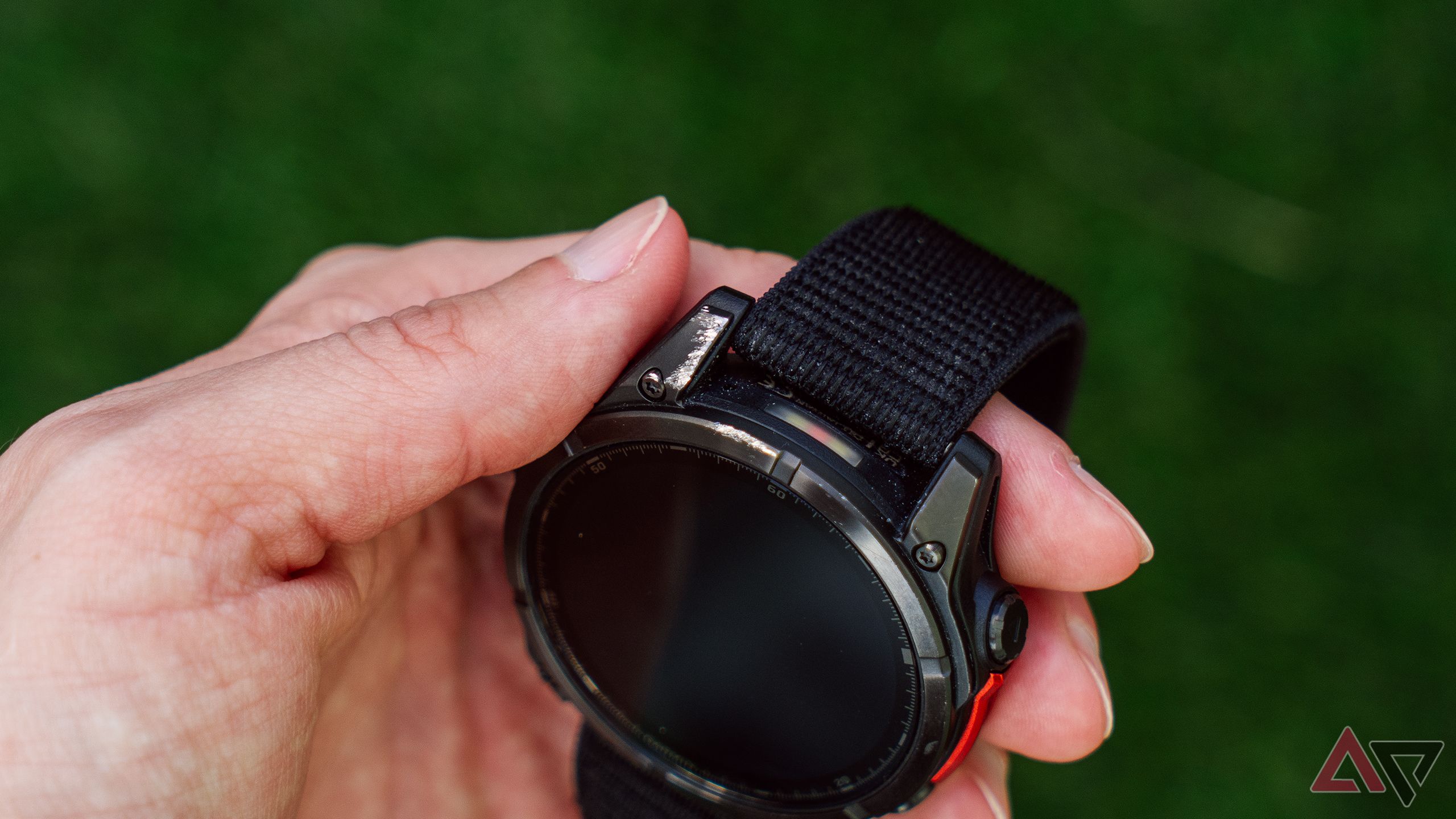 A hand holds a scratched Garmin Fenix 8 AMOLED above a blurred green background. 