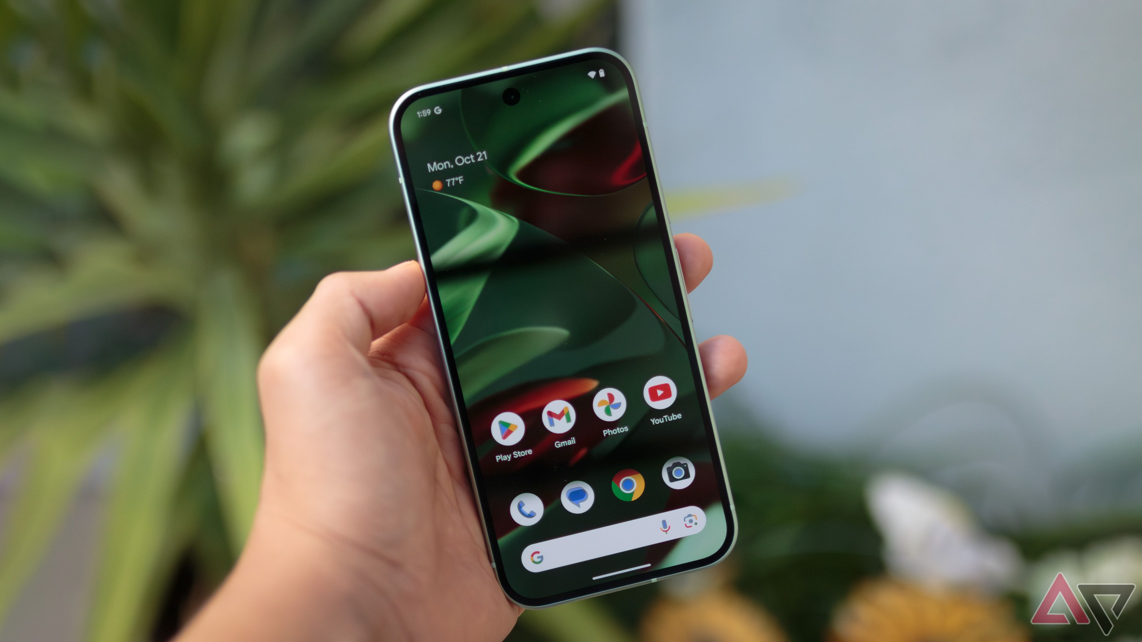 The Google Pixel 9 being held in front of greenery with the default green wallpaper