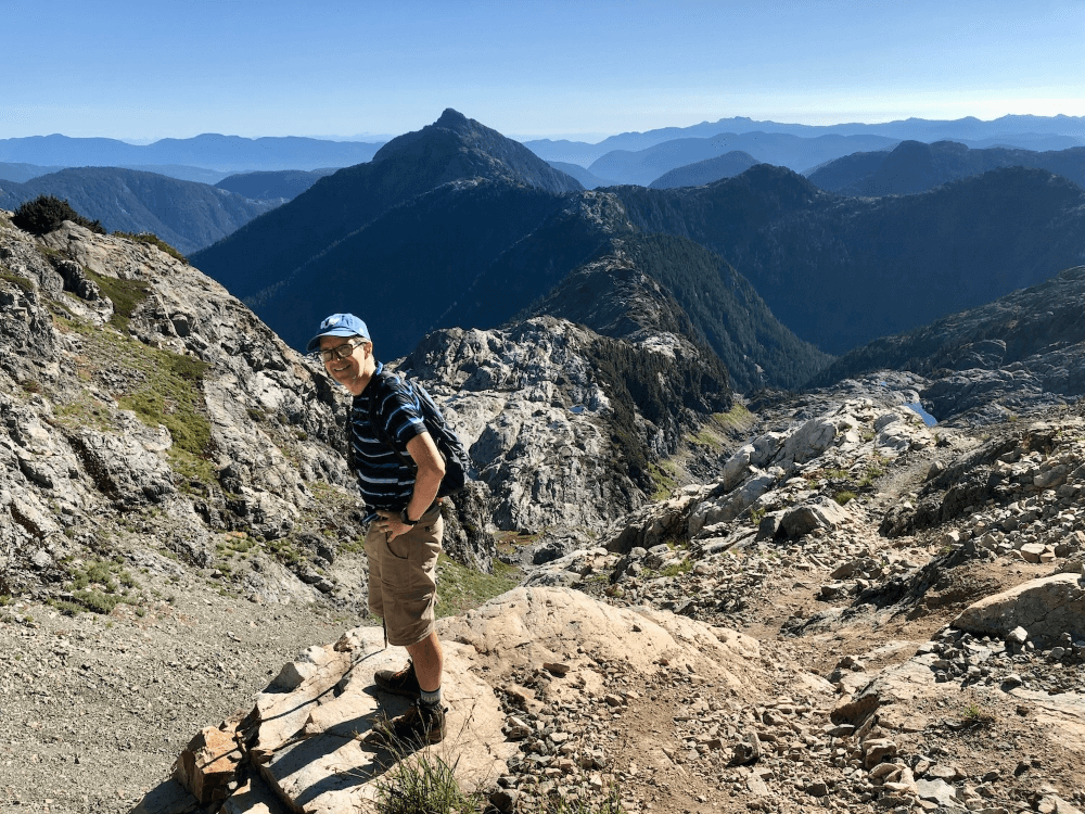 Michael McCullough stands on a hiking trail in front of mountains.