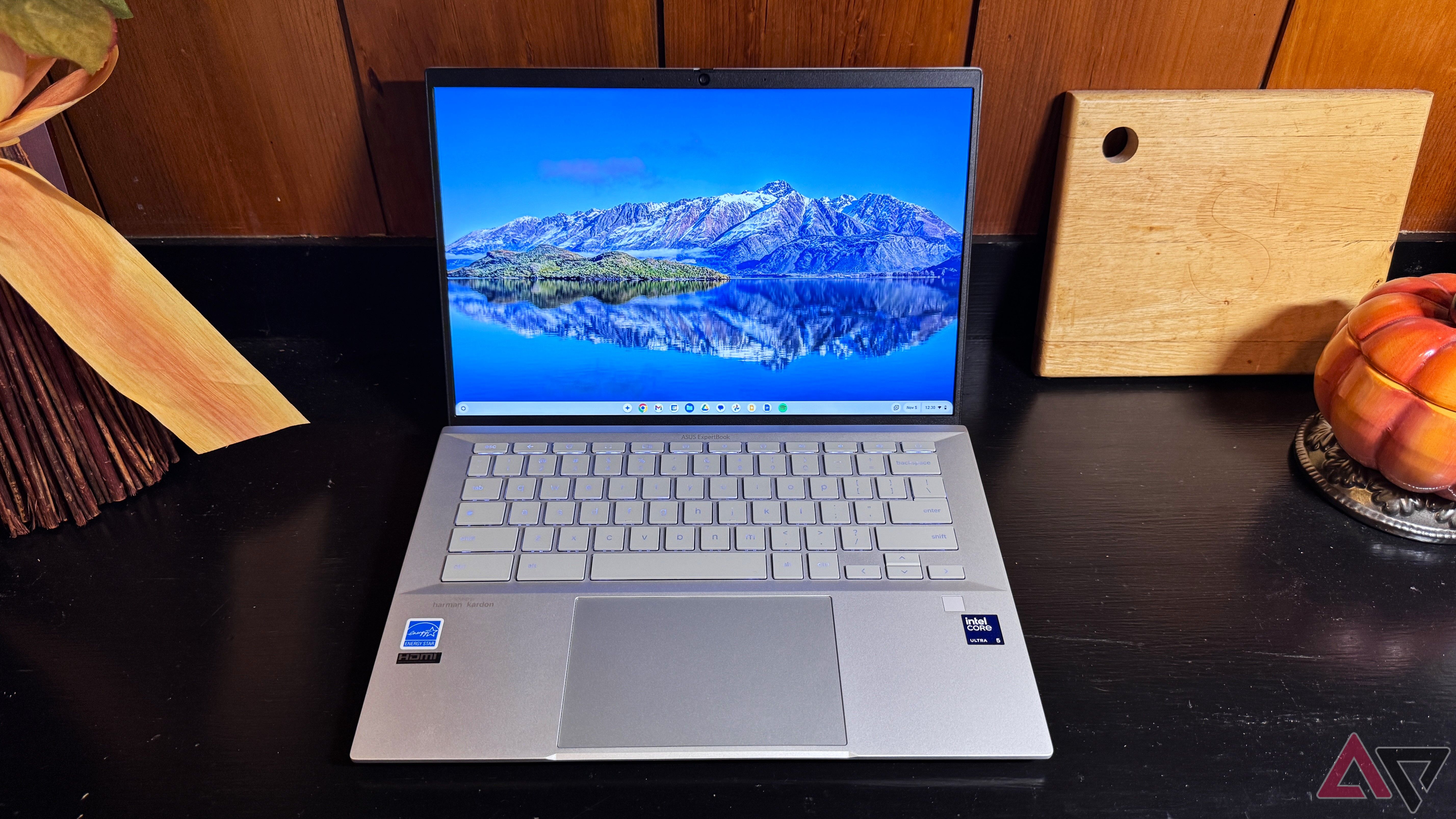 Asus Chromebook Plus CX54 on a black surface with a light brown background next to a wooden cutting board.