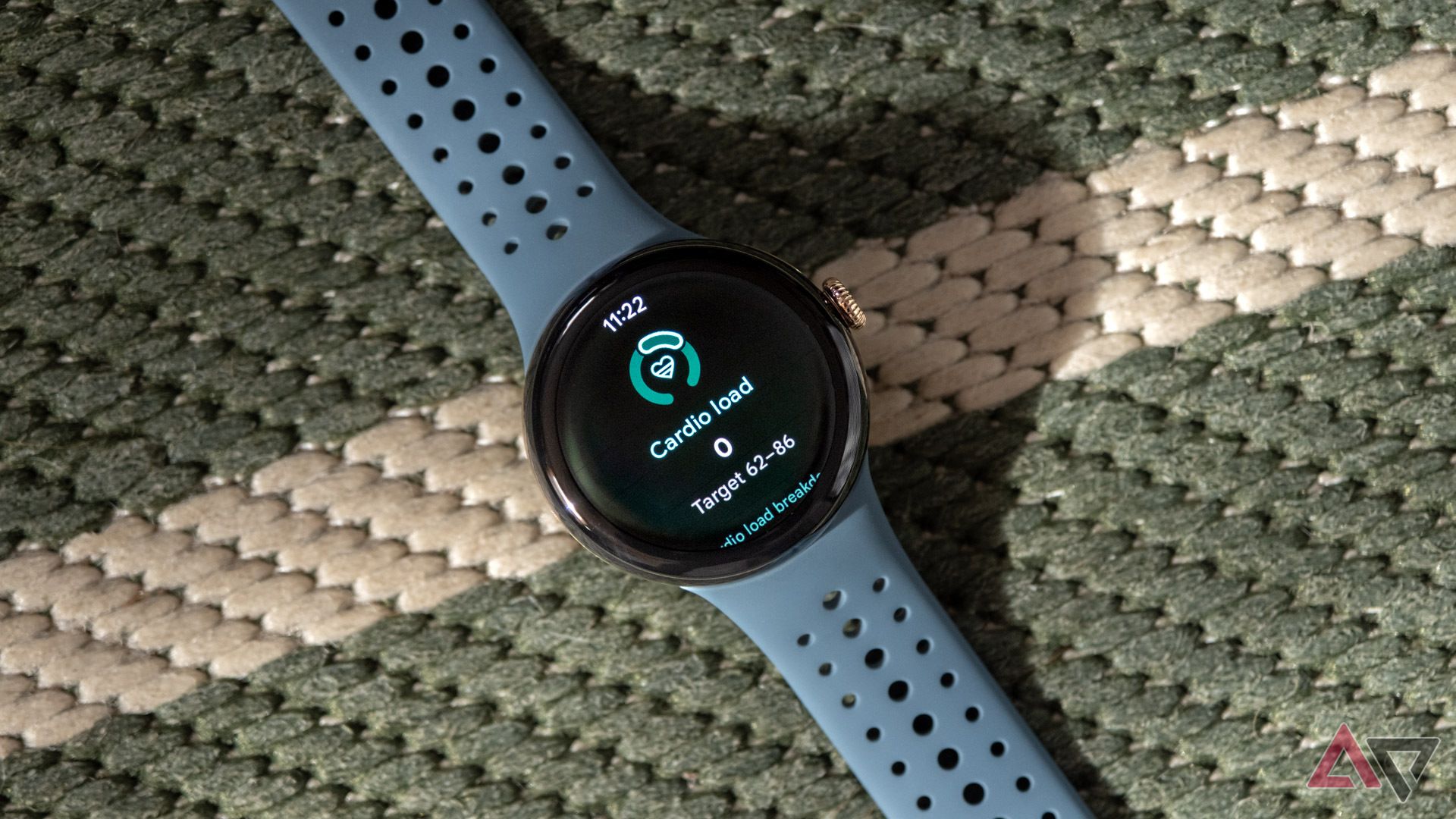 The Google Pixel Watch 3 sits on a green and white woven surface with the Cardio Load feature on the display. 