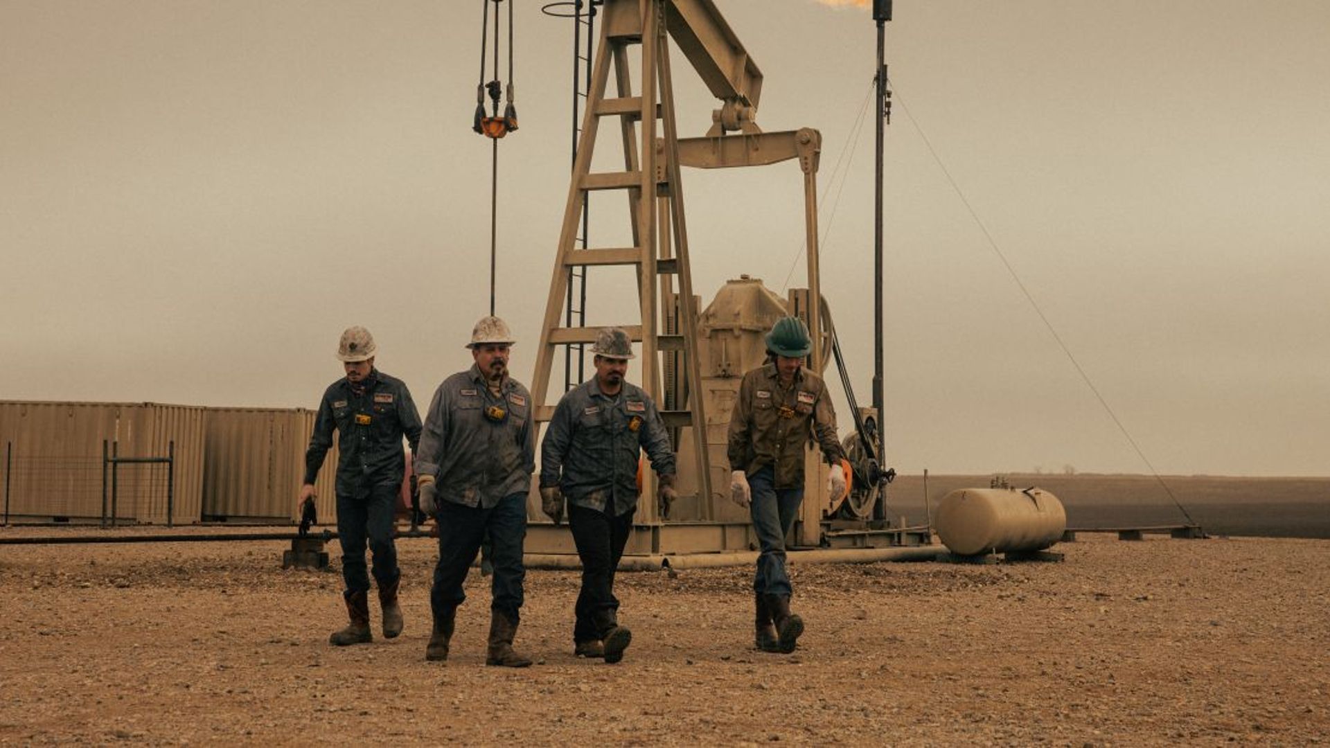 Oil workers walk by a derrick in Landman