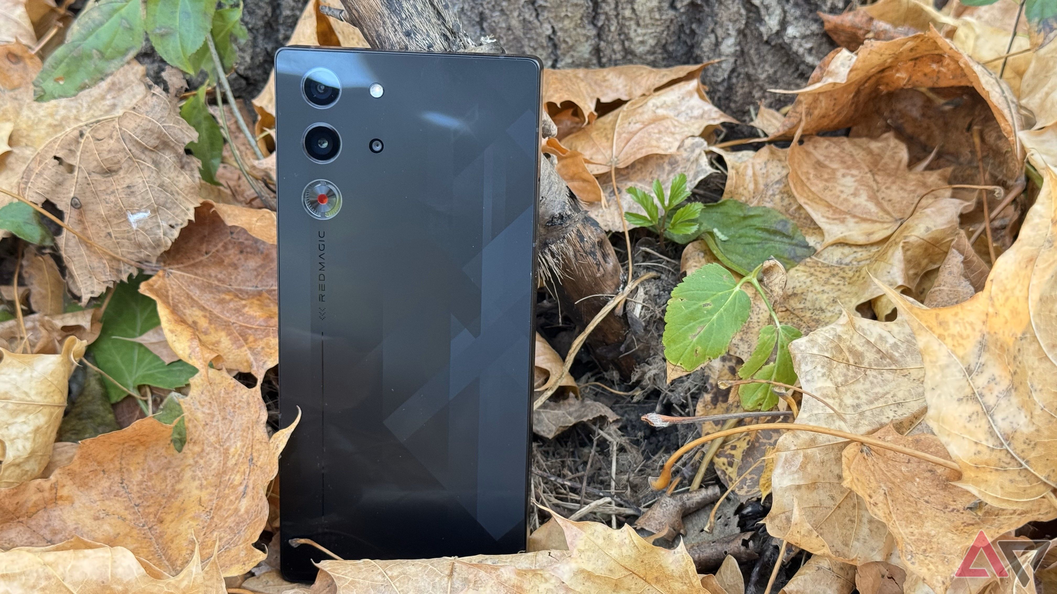 A black RedMagic 10 Pro phone leaning against a tree and surrounded by brown leaves.