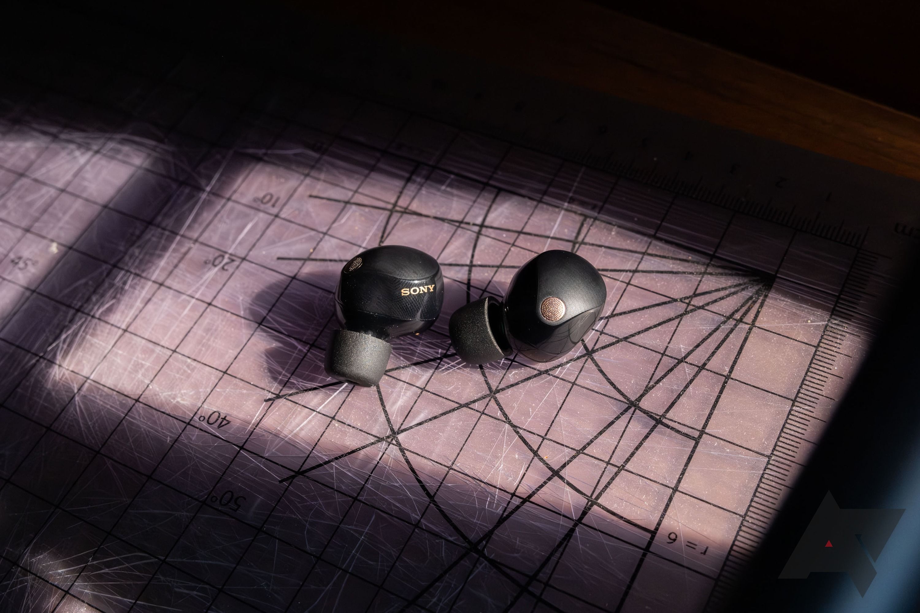 sony wf 1000 xm5 earbuds laying in a beam of light with shadows around them