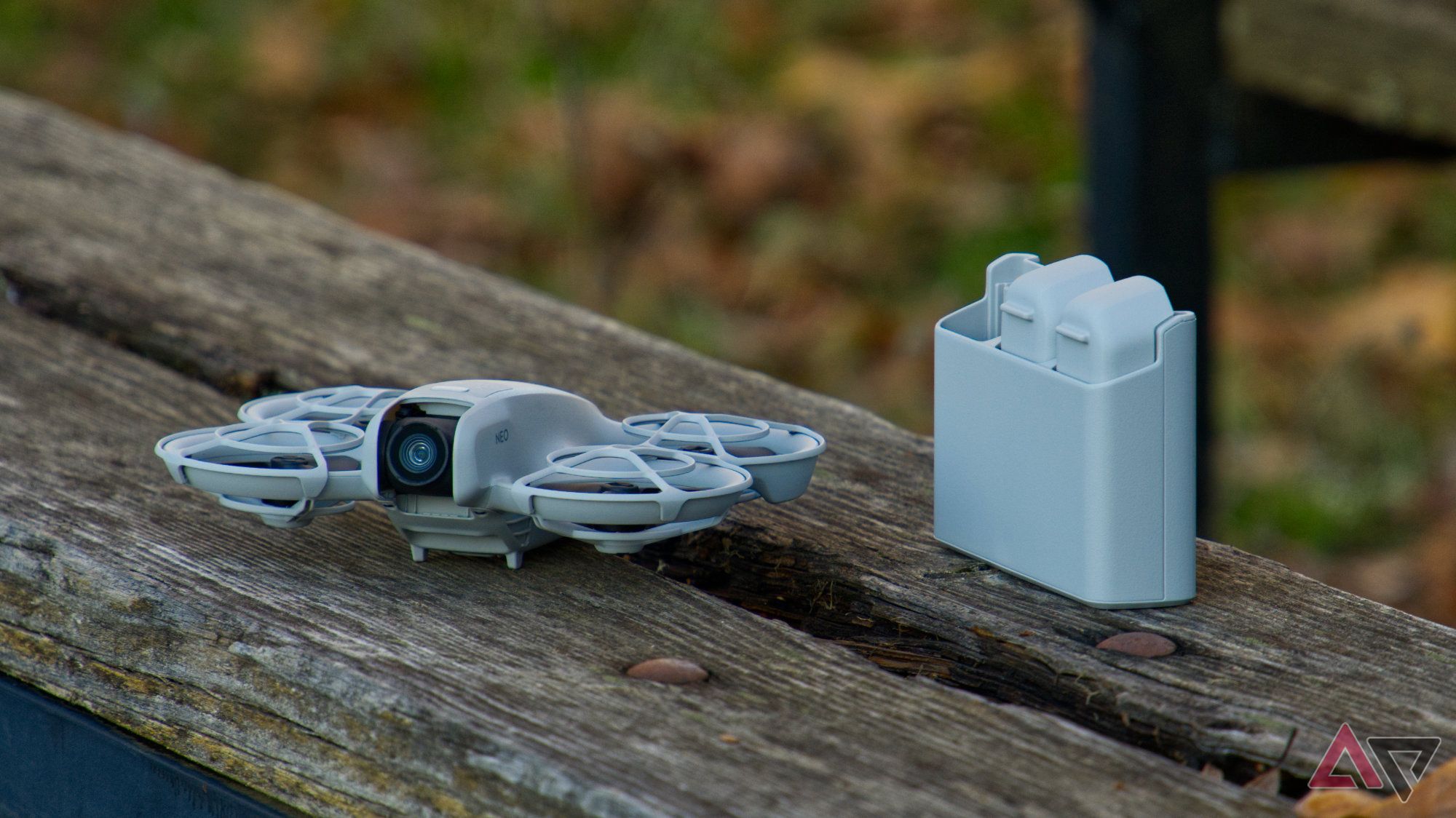 DJI Neo on a wooden bench next to the battery charger with two batteries inside