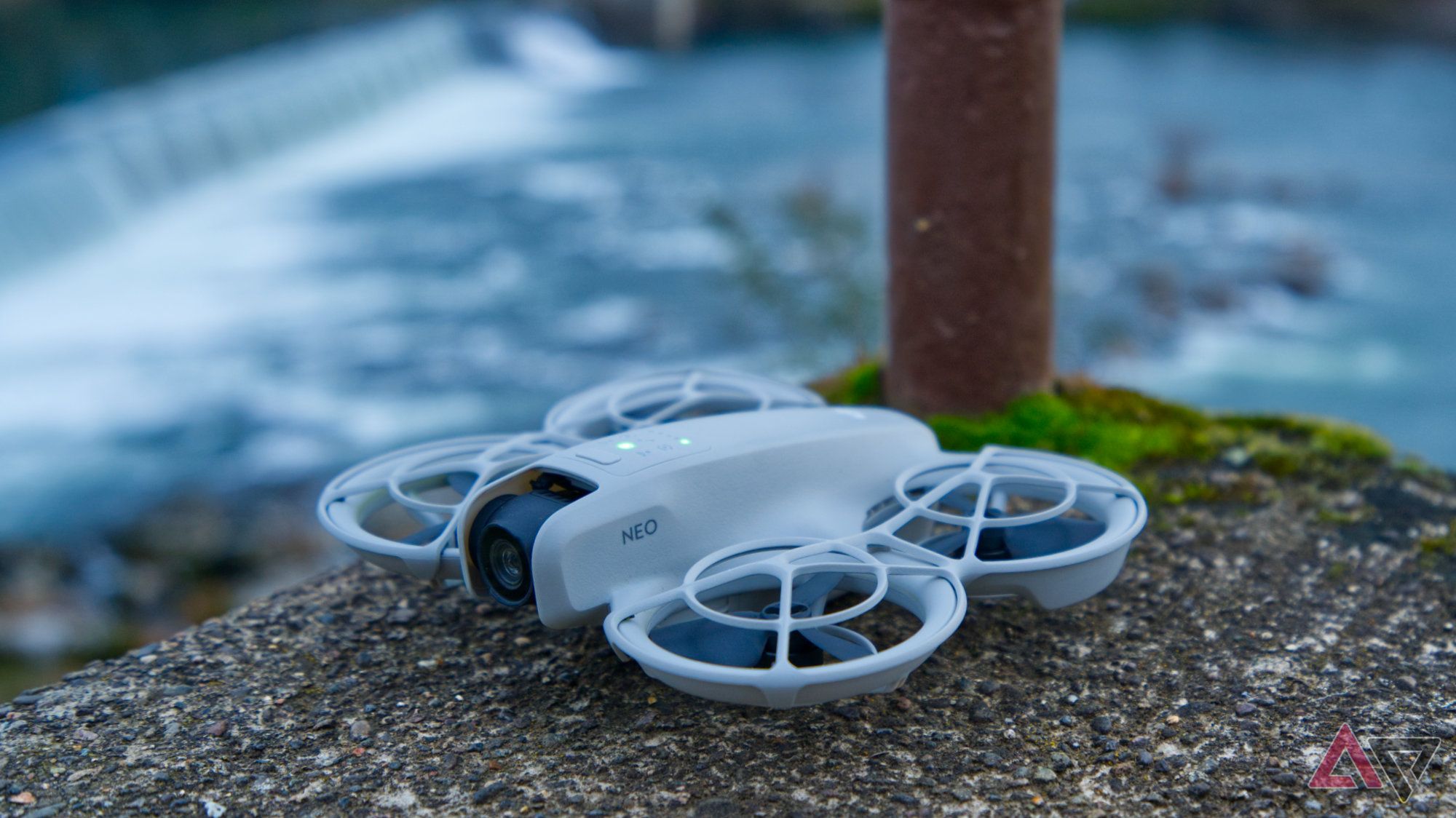 DJI Neo on a concrete step overlooking a river and dam in the background