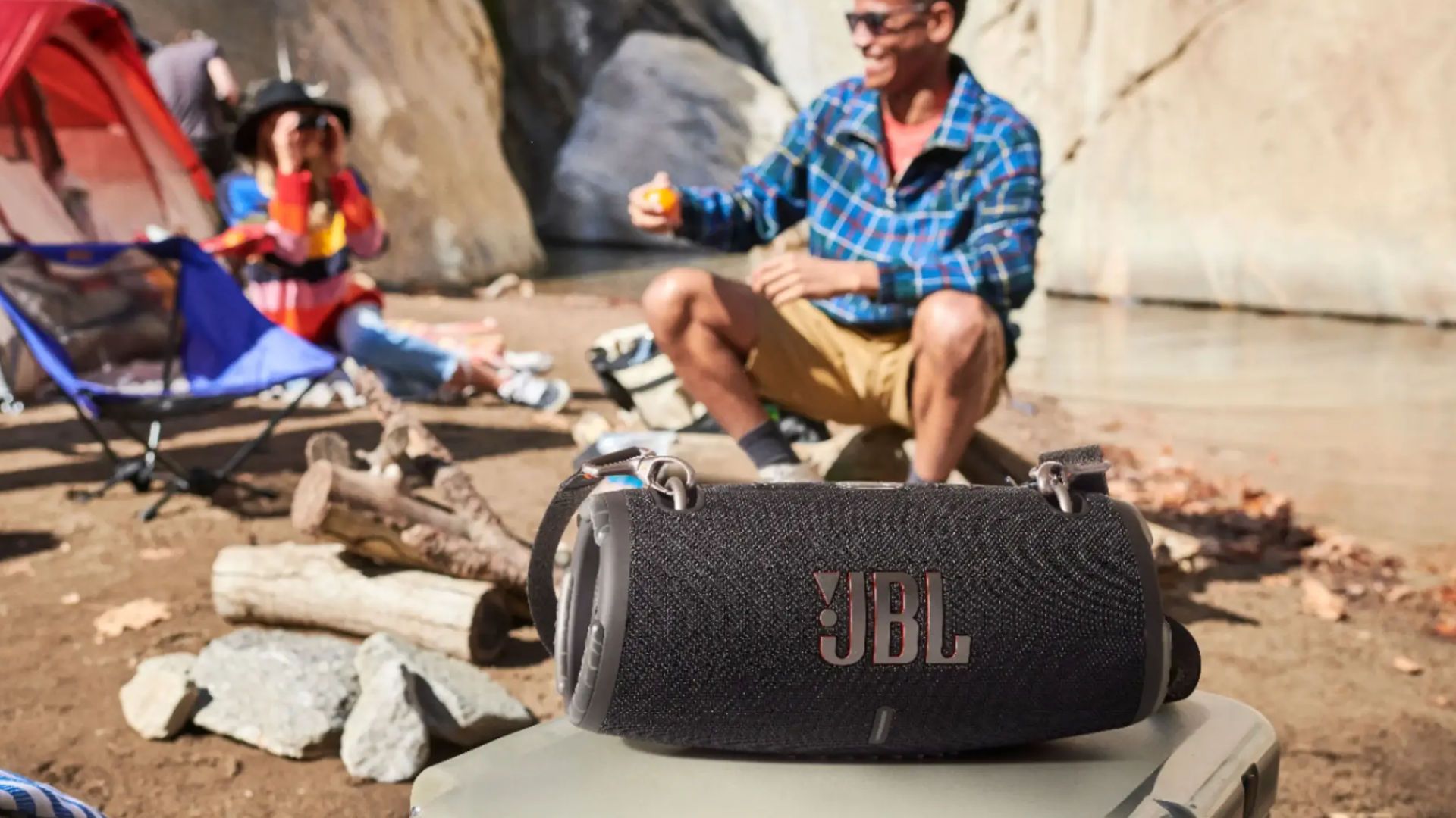 A JBL Xtreme 3 Bluetooth speaker with people camping in the background.