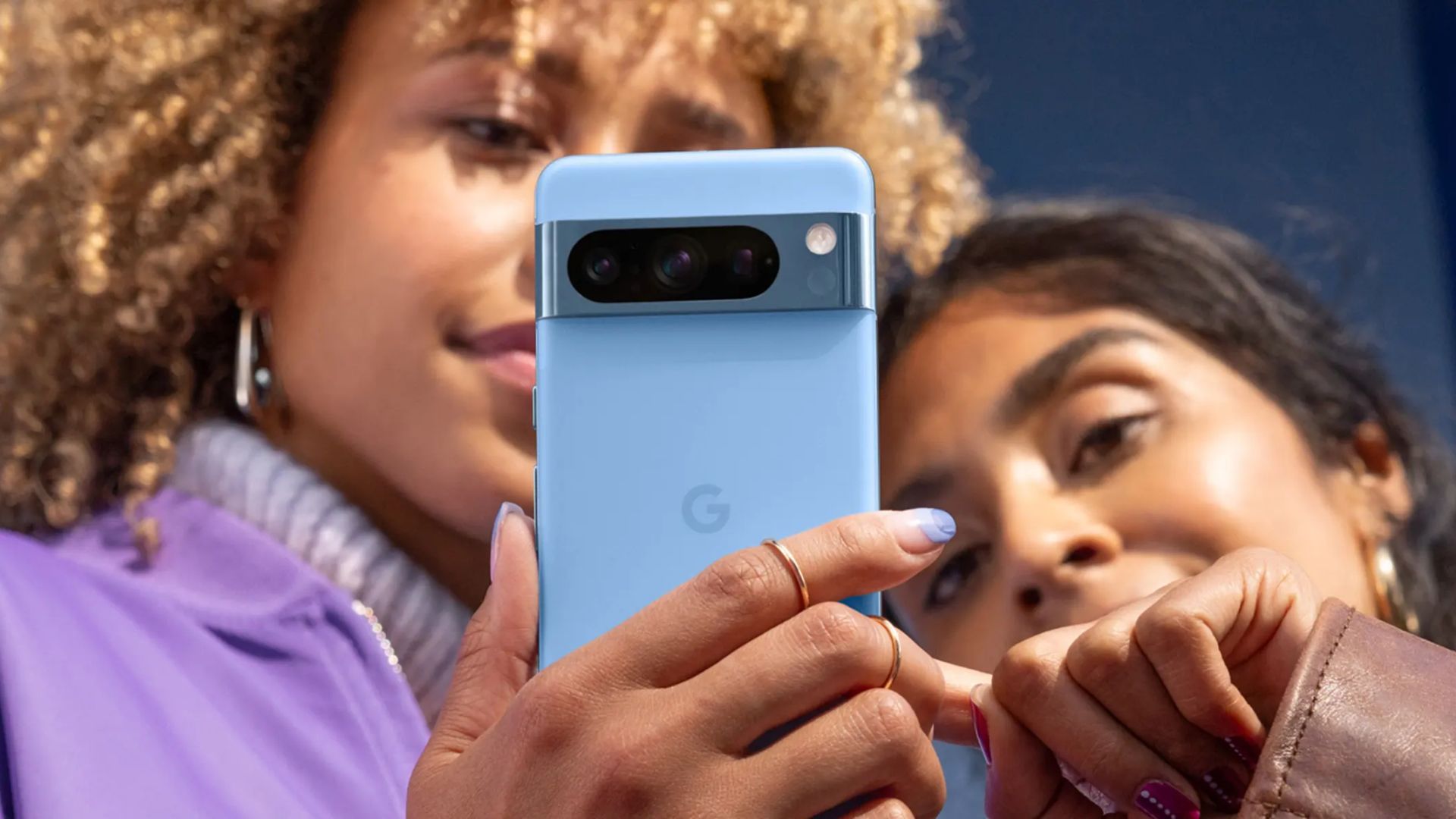 A person holds a blue Pixel 8 Pro while another taps on it